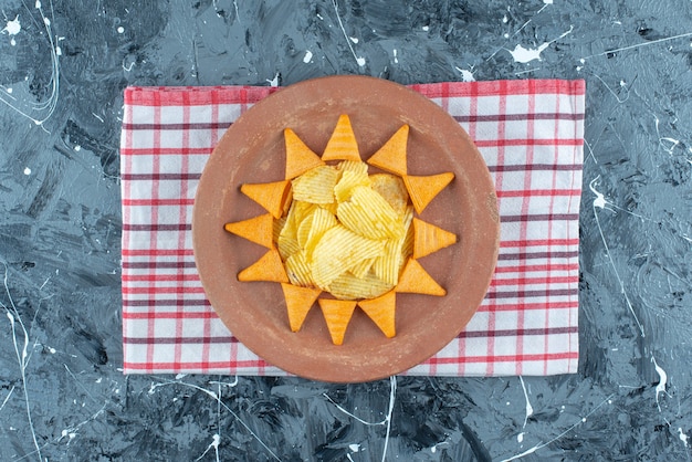 Chips de queijo e chips de cone em um prato no pano de prato em mármore.