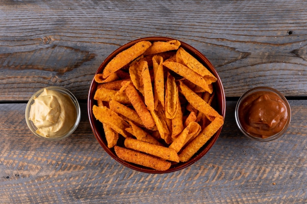 Chips de vista superior com sauses em tigelas na horizontal de madeira marrom