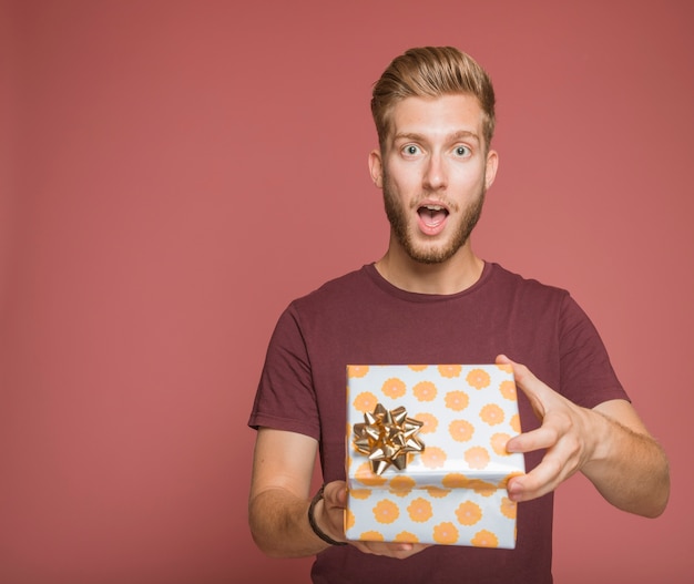 Chocado jovem abrindo uma caixa de presente floral com laço dourado