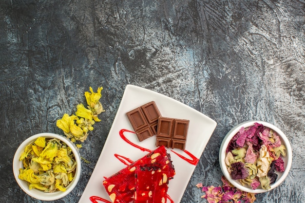 Chocolate em prato branco perto de tigelas de flores secas em solo cinza