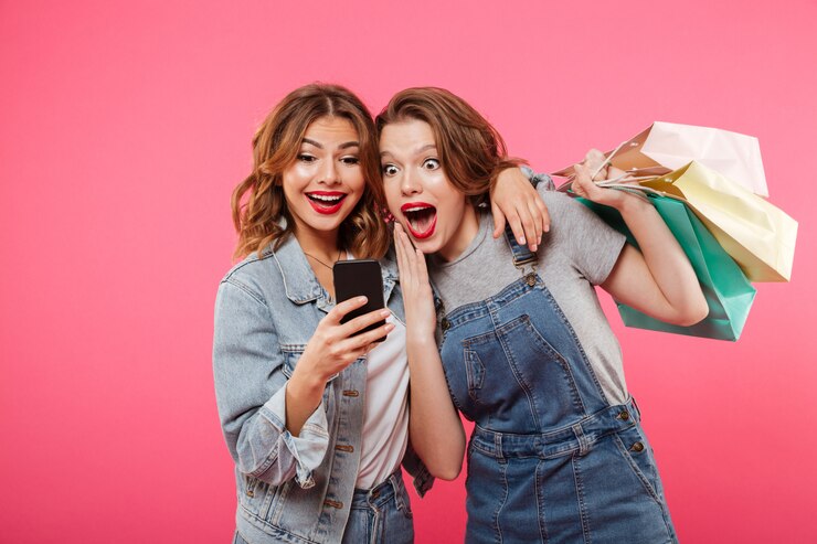 Foto grátis chocou dois amigos de mulheres segurando sacolas usando telefone celular.