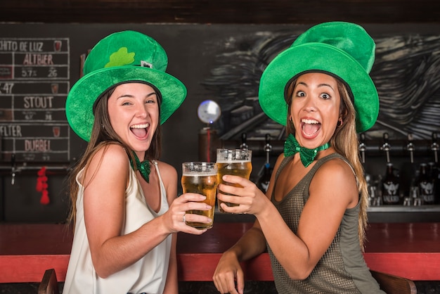 Chorando mulheres felizes em chapéus de saint patricks clanging óculos de bebida no balcão de bar