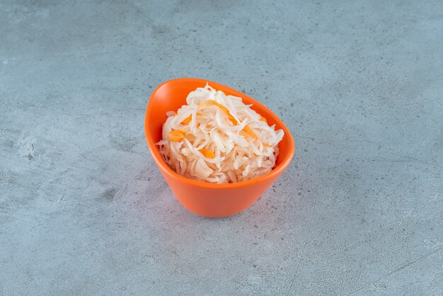 Chucrute fermentado com cenouras em uma tigela de plástico na superfície azul