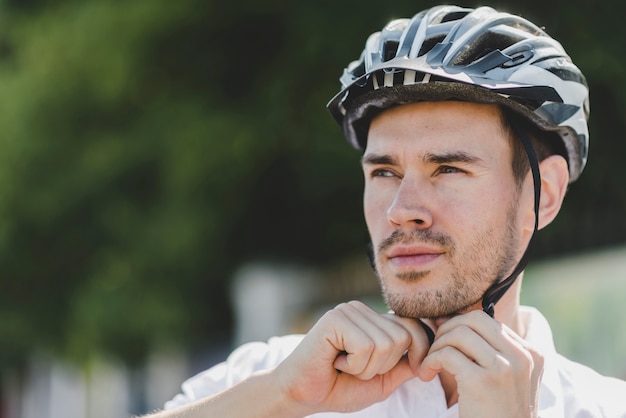 Ciclista masculina considerável usando capacete olhando para longe