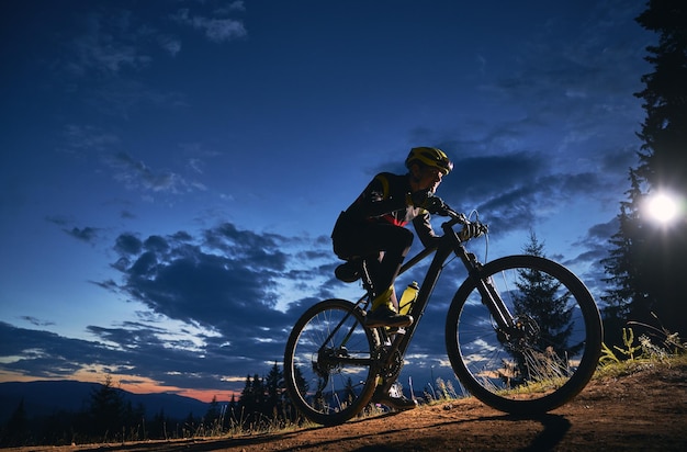 Foto grátis ciclista sentado na bicicleta sob o céu noturno nublado