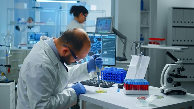 Cientista colocando amostra de sangue de tubo de ensaio com micropipeta em placa de Petri, analisando reação química
