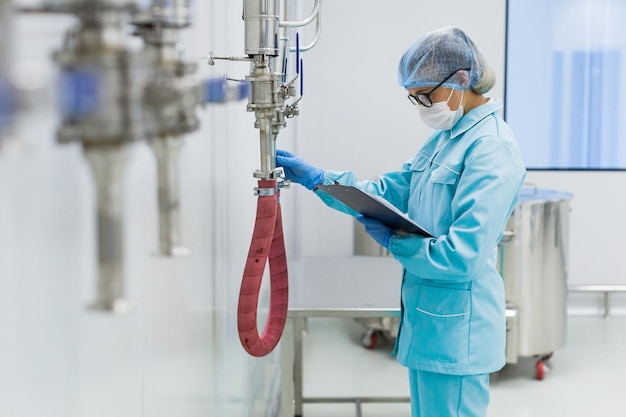 Cientista da frente em traje de laboratório azul verifica as leituras da barra de aço do medidor de pressão no foco de fundo no cientista