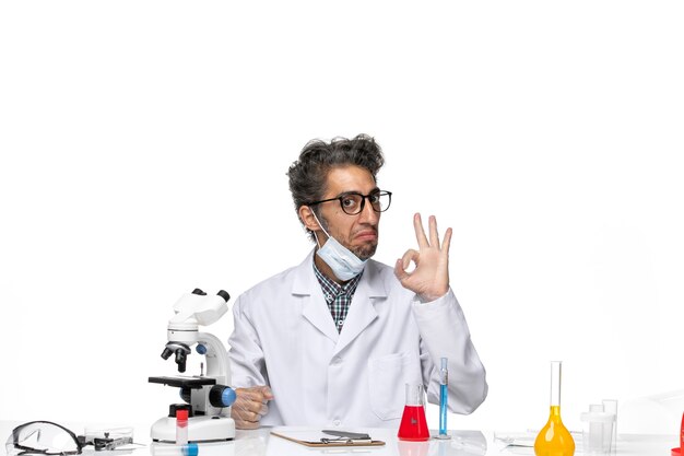 Cientista de meia-idade com vista frontal em um terno especial sentado ao redor da mesa com soluções