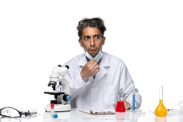 Cientista de meia-idade de vista frontal em traje médico branco sentado ao redor da mesa com soluções
