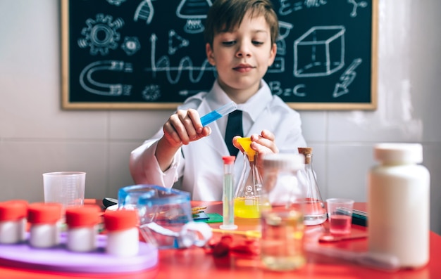 Cientista de menino brincando com líquidos químicos contra lousa com desenhos. foco seletivo nas mãos. Foto Premium