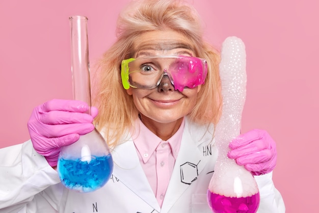 Foto grátis cientista faz pesquisa experimento químico segura dois frascos de vidro com reagentes mistos usa óculos e jaleco branco isolado em rosa