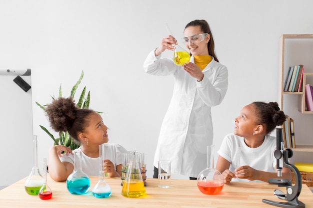 Cientista fêmea ensinando química de meninas enquanto segura o tubo com poção