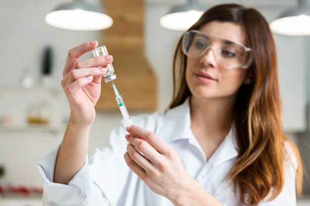 Cientista feminina com óculos de segurança segurando uma seringa com vacina no laboratório