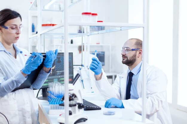 Cientista jovem olhando pensativo para a solução química em tubos de ensaio. Equipe de químicos químicos trabalhando juntos em um laboratório de microbiologia estéril, fazendo pesquisas.