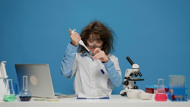 Foto grátis cientista pateta insano usando micro pipeta e tubo de ensaio na frente da câmera, agindo como louco no estúdio e fazendo expressões faciais tolas. divertido químico feminino engraçado com cara suja.