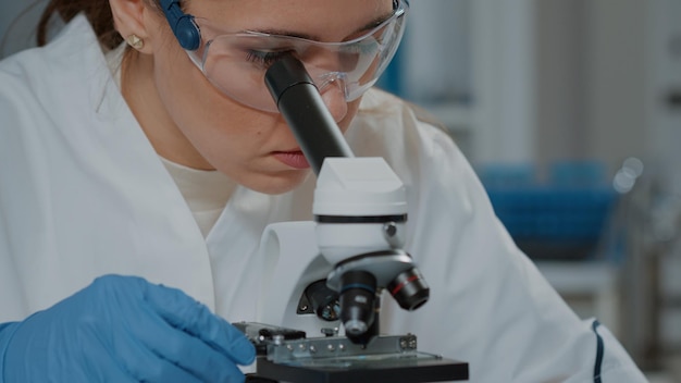 Cientista que olha através de lentes microscópicas para trabalhar em experimentos, usando microscópio para analisar DNA com foco seletivo em laboratório. Biólogo que trabalha com lupa. Fechar-se