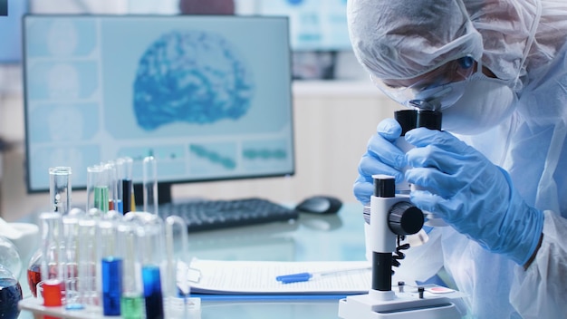 Cientista químico pesquisador médico analisando amostra de DNA usando microscópio médico, desenvolvendo vacina contra coronavírus durante experimento de bioquímica em laboratório de hospital. Conceito de medicina