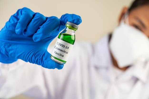 Cientistas usando máscaras e luvas, carregando frascos com vacinas para proteger Covid-19