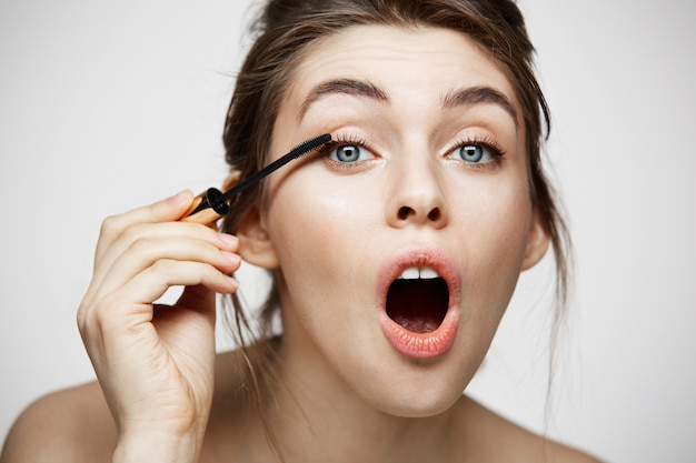 Cílios bonitos bonitos da tintura da menina com a boca aberta que olha a câmera sobre o fundo branco. Conceito de saúde e cosmetologia de beleza.