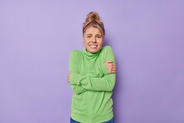 Cintura para cima foto de uma jovem descontente sente congelamento cruza os braços e tenta aquecer arrepios durante o tempo frio usa gola olímpica verde isolada sobre fundo roxo precisa colocar um casaco.