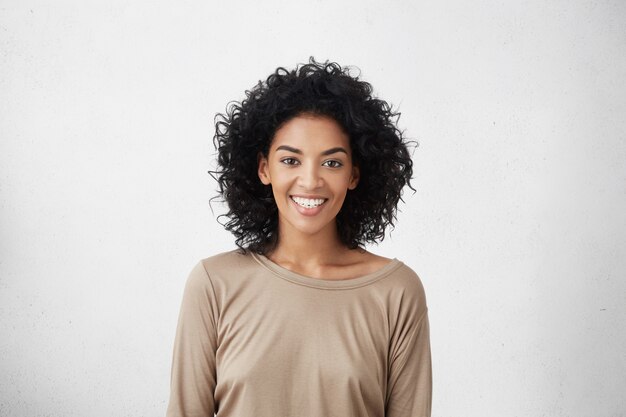 Cintura para cima o retrato de uma fêmea jovem de raça mista, vestida casualmente, com cabelos cacheados, sorrindo alegremente durante a audição para o papel em séries de TV, sentindo-se excitada e muito nervosa, tentando impressionar o diretor