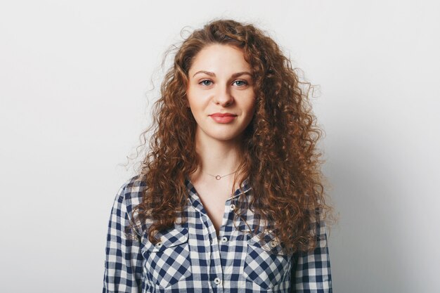 Cintura para cima o retrato de uma mulher linda tem penteado encaracolado vestido casualmente, isolado sobre o branco