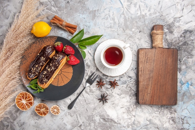 Éclairs de chocolate saborosos com uma xícara de chá no biscoito de sobremesa de bolo de biscoitos brancos