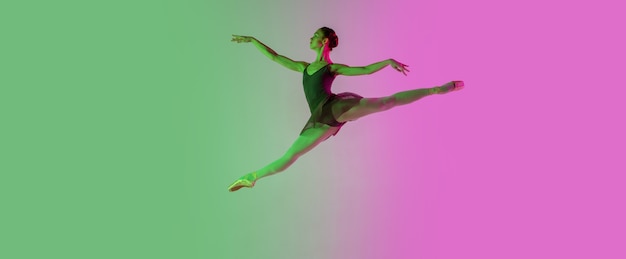 Claro. Dançarina de balé jovem e graciosa isolada na parede verde-rosa gradiente em neon. Arte, movimento, ação, flexibilidade, conceito de inspiração. Bailarina flexível, saltos leves.