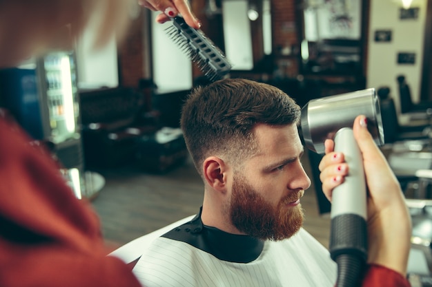 Cliente durante o barbear na barbearia. Barbeiro feminino no salão. Igualdade de gênero. Mulher na profissão masculina.