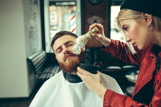 Foto grátis cliente durante o barbear na barbearia. barbeiro feminino no salão. igualdade de gênero. mulher na profissão masculina.