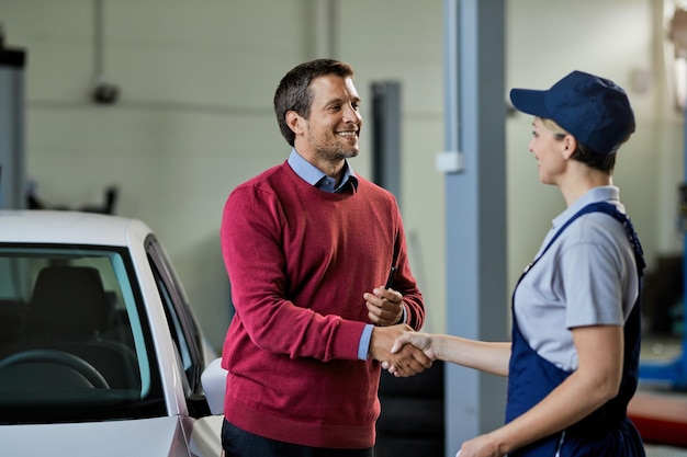 Cliente satisfeito apertando as mãos com mecânico de automóveis feminino em uma oficina