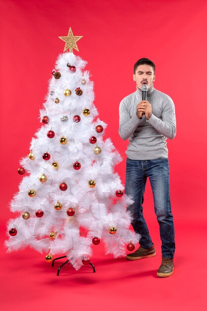 Clima de ano novo com cara positiva vestida de jeans em pé perto da árvore de Natal decorada