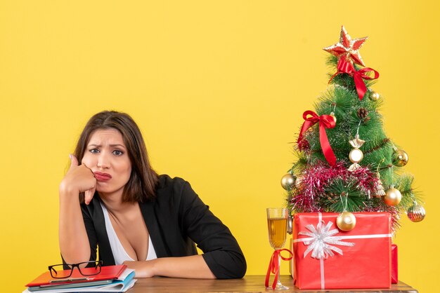 Clima de ano novo com uma linda mulher de negócios insatisfeita, confusa com alguma coisa e sentada à mesa do escritório