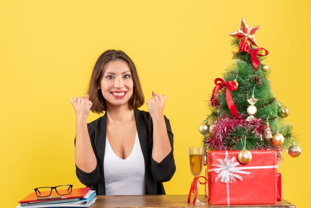 Clima de ano novo com uma linda mulher sorridente, feliz e sorridente, mostrando sua força e sentada em uma mesa no escritório