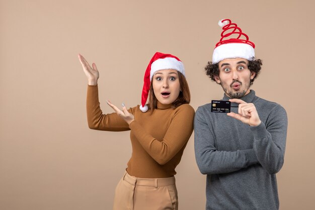 Clima de natal com casal animado satisfeito surpreso com chapéu de papai noel vermelho mostrando cartão do banco