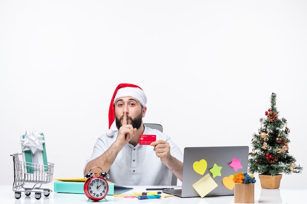 Foto grátis clima de natal com jovem adulto com chapéu de papai noel e olhando para o cartão do banco e fazendo gesto de silêncio no escritório