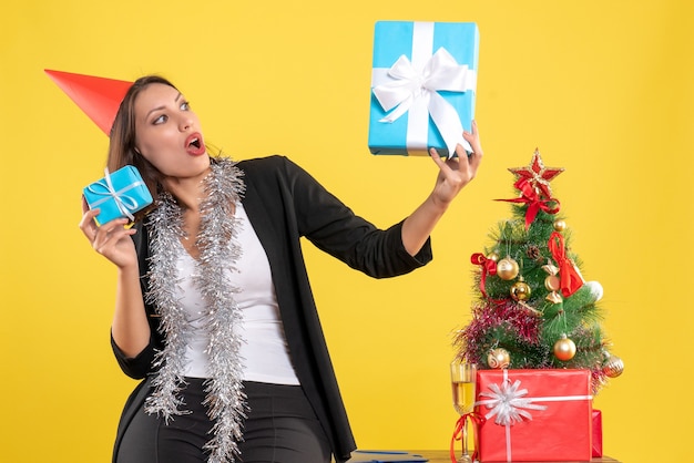 Clima de Natal com linda senhora surpresa com chapéu de Natal segurando presentes no escritório em amarelo