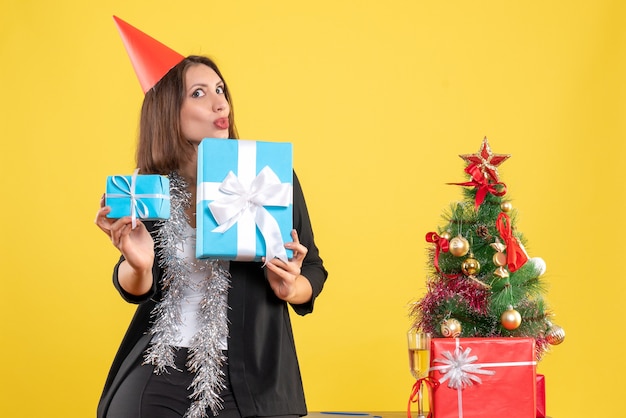 Clima de natal com surpresa positiva linda senhora com chapéu de natal segurando presente no escritório em amarelo