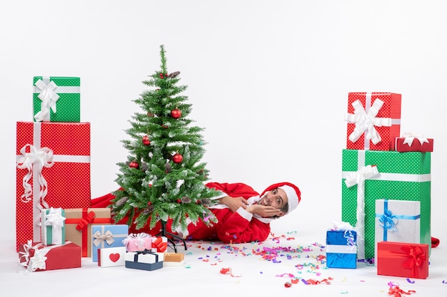 Clima festivo de feriado com o papai noel deitado atrás da árvore de natal perto de presentes em cores diferentes no banco de imagens de fundo branco