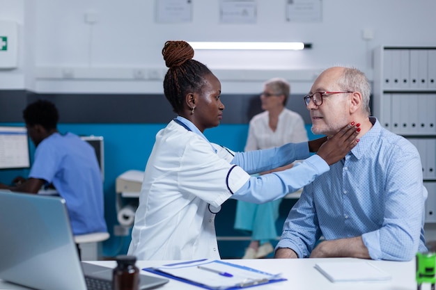 Clínica especializada otologista examinando homem sênior enquanto toca seu pescoço. Trabalhador de clínica consultando paciente idoso tocando seu pescoço procurando sintomas de doença