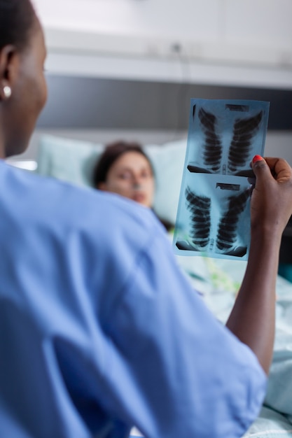 Foto grátis close da enfermeira afro-americana analisando o raio x dos pulmões, verificando o paciente da mulher doente da recuperação do healdcare.