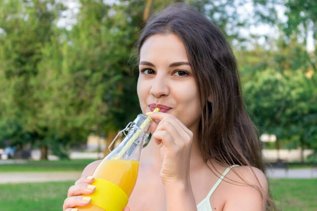 Close da menina bonita com uma garrafa de suco fresco. mulher saudável está posando com limonada. nutrição dietética com suco desintoxicante.
