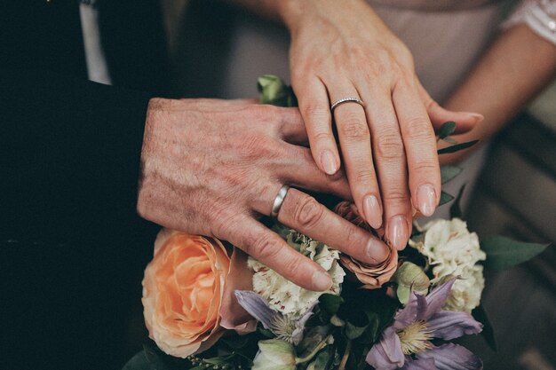 Close das mãos de um casal segurando um ao outro sobre um buquê