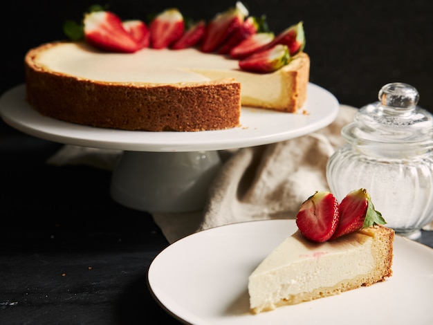 Close de ângulo alto de um cheesecake de morango em um prato branco e um fundo preto