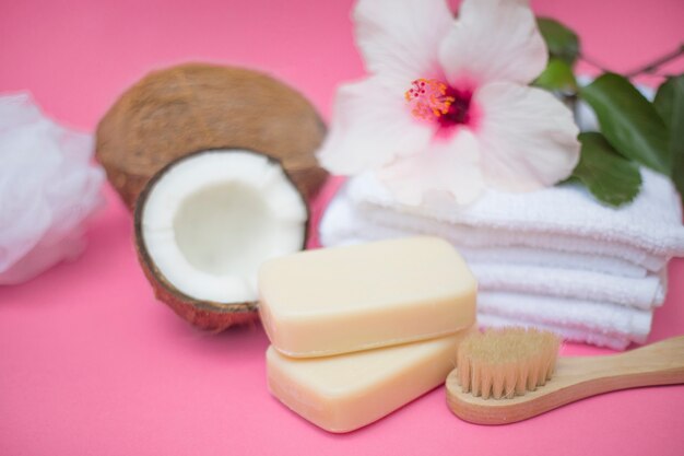 Close de coco; Sabonete; escova; flor e toalhas no pano de fundo rosa