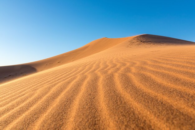 Close de ondulações de areia em dunas de areia em um deserto contra um céu azul claro
