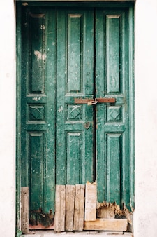 Close de portas de madeira verdes gastas trancadas com fundo quebrado e tábuas na entrada