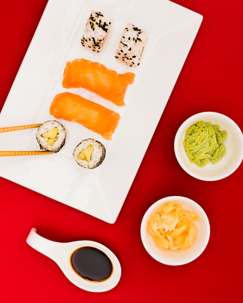 Close de rolos de sushi e sashimi servidos com wasabi; calda de gengibre e molho de soja