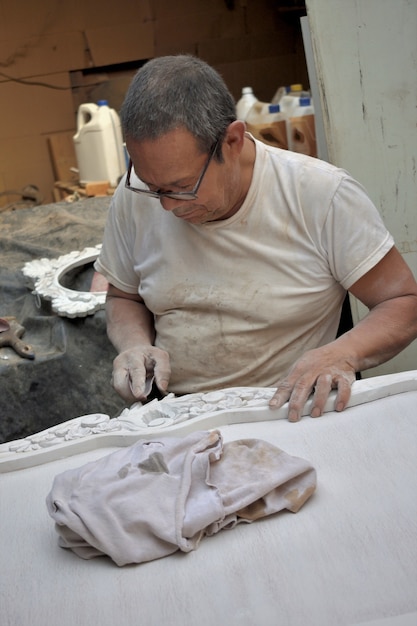 Close de um artesão de madeira esculpindo um desenho decorativo em móveis de madeira em sua oficina