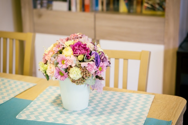 Close de um buquê de flores coloridas em um vaso branco sobre uma mesa de madeira